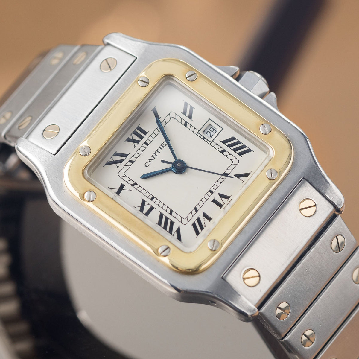 Close view of a two-tone Santos Carrée 2961 with its white dial, black Roman numerals and minute track, blued sword hands and date window. · Photo: Bulang & Sons · © Bulang & Sons, used with permission · Source: https://bulangandsons.com/products/cartier-santos-carree-steel-and-gold-automatic-movement-w1736